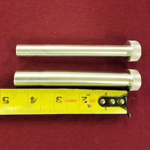 Puede incluir: Dos varillas de metal plateado con extremos moleteados, que miden aproximadamente 7,6 cm de largo, se colocan sobre una cinta métrica Stanley amarilla.