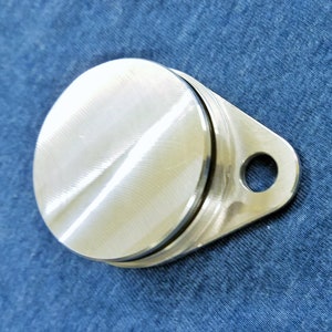 May include: A silver metal cap with a round top and a small hole on the side. The cap has a brushed finish.