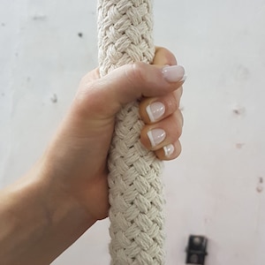 Può includere: Primo piano di una mano che afferra una corda spessa di colore bianco. La corda è intrecciata in un motivo di treccia stretto. La mano ha lo smalto bianco con una sottile linea bianca sulla punta di ogni unghia.