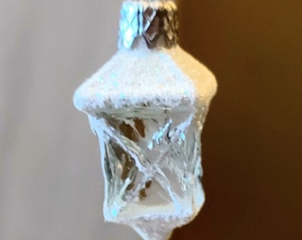 Pode incluir: Um enfeite de Natal de vidro branco em forma de lanterna com acabamento fosco e topo prateado.