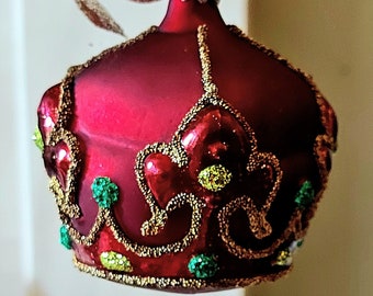 May include: A red glass Christmas bauble shaped like a crown with gold and green accents.