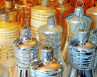 May include: A collection of vintage glass Christmas decorations in gold, silver, and clear glass. The decorations are shaped like bells and have a textured, sparkly finish.