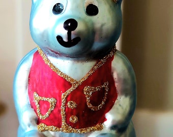 May include: A blue glass Christmas bauble shaped like a bear wearing a red waistcoat with gold glitter accents.