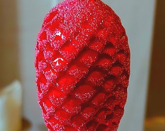 May include: A red glass Christmas bauble shaped like a pine cone with a silver top.