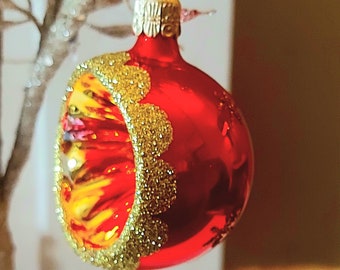 May include: A red glass Christmas bauble with a gold glitter trim and a yellow and orange design.