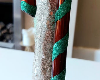 May include: A red and green candy cane ornament with glitter. The candy cane is made of glass and has a shiny finish.