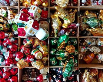 May include: A collection of vintage glass Christmas baubles in a wooden box. The baubles are arranged in rows and include a variety of shapes, colours, and designs, including houses, fish, and pinecones.