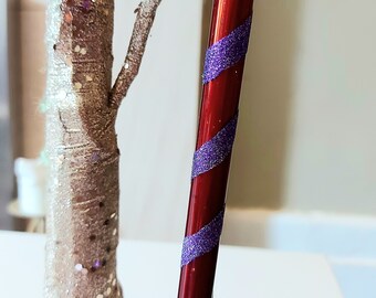 May include: A red and purple candy cane Christmas ornament with glitter.