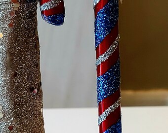 May include: A red and blue candy cane with silver glitter. The candy cane is striped with red and blue and has a silver glitter finish.