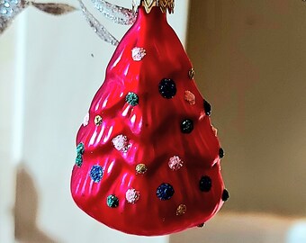 Pode incluir: Um enfeite de árvore de Natal de vidro vermelho com uma parte superior dourada e bolinhas verdes, azuis e rosas.
