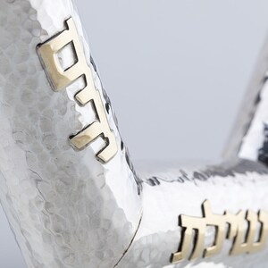May include: A silver and gold Kiddush cup with Hebrew lettering. The cup is hammered and has a textured surface.