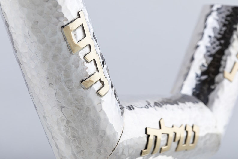 May include: A silver and gold Kiddush cup with Hebrew lettering. The cup is hammered and has a textured surface.