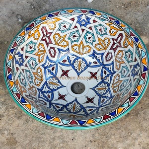 May include: A white ceramic sink with a blue, red, yellow, and green geometric pattern. The sink has a round shape and a drain hole in the center.