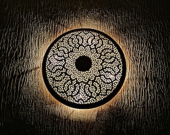 May include: A round, decorative wall light with a intricate, cut-out design. The light is made of metal and has a warm, golden glow.