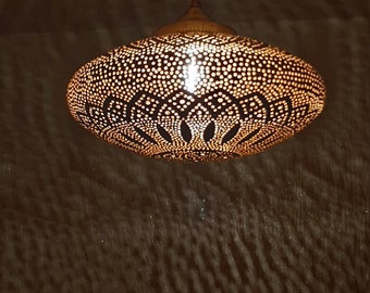 May include: A gold-toned metal pendant light fixture with a round, perforated shade. The shade has a decorative pattern of circles and swirls. The light is hanging from a chain.