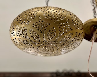 May include: A gold-toned, round, hanging light fixture with intricate cut-out designs. The light fixture is suspended from a chain.