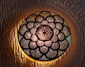 May include: A round, metal wall sconce with a decorative, intricate pattern of cut-outs. The sconce is lit and casts a warm glow.