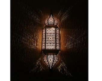 May include: A decorative Moroccan lantern with intricate metalwork and a warm glow. The lantern is hanging on a wall with a textured surface. The text "Moroccan bazaars" is visible at the bottom of the image.
