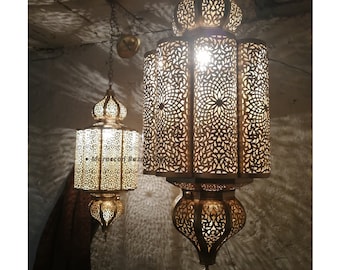 May include: Two ornate gold Moroccan pendant lights with intricate cut-out designs. The larger light is hanging from the ceiling and the smaller light is hanging below it.