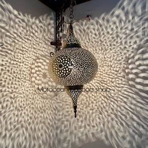 May include: A brass Moroccan pendant light with intricate cut-out designs. The light casts a beautiful pattern on the wall behind it.