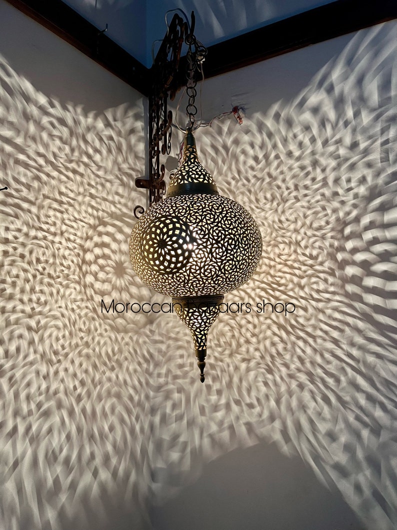 May include: A brass Moroccan pendant light with intricate cut-out designs. The light casts a beautiful pattern on the wall behind it.