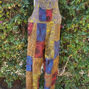 May include: Patchwork overalls with a multi-colored design featuring mushrooms, geometric patterns, and other nature-inspired motifs. The overalls are made of a soft, comfortable fabric and have adjustable straps.