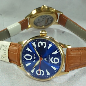 May include: Two gold-toned Paketa watches with blue faces and white numerals. The watch bands are brown leather. One watch is in focus, displaying the brand name and the text "СДЕЛАНО В СССР". The other watch is out of focus.