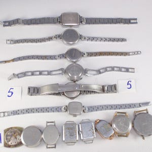 May include: A collection of vintage wristwatches with silver-toned metal bands and watch faces. The watches have various shapes, including round, square, and rectangular. Some watches are complete, while others are missing parts. Numbers 4 and 5 are written on small white cards.