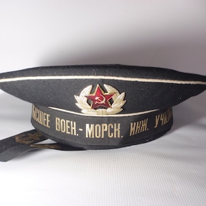 May include: A black sailor hat with a white band and a red star with a hammer and sickle emblem. The hat has a gold band with the text "ВЫСШЕЕ ВОЕН. - МОРСК. ИНЖ. УЧ. " in Cyrillic.
