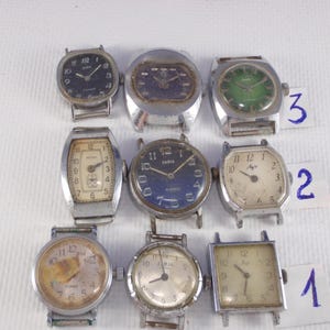 May include: Nine vintage wristwatches with various face designs and metal bands are displayed. The watch faces feature different colors, including black, green, and cream. Some watches have Arabic numerals, while others have a minimalist design.