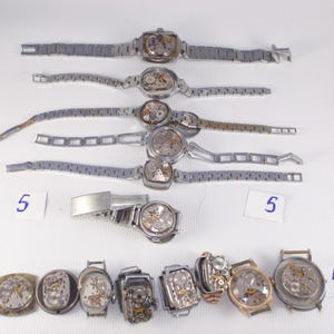 May include: A collection of vintage wristwatches, some with exposed mechanical movements. The watches have silver-toned metal bands and various case shapes, including square and rectangular. Some watches are missing parts. Numbers 4 and 5 are written on small white cards.