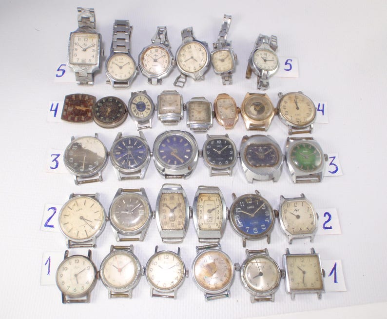May include: A collection of vintage wristwatches with various face shapes and band styles. The watches feature silver, gold, and brown tones, with some displaying Roman numerals and others Arabic numerals. The collection includes both round and rectangular watch faces.