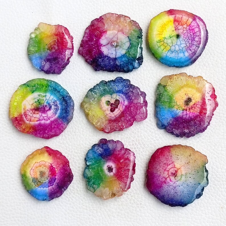 May include: Nine rainbow agate slices with a white center and a variety of colors, including red, orange, yellow, green, blue, and purple.