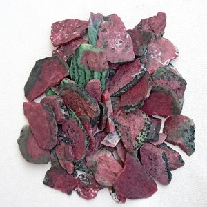 Może przedstawiać: Stosik r&oacute;żowych i zielonych odłamk&oacute;w kamieni szlachetnych. Odłamki mają nieregularny kształt i szorstką fakturę.