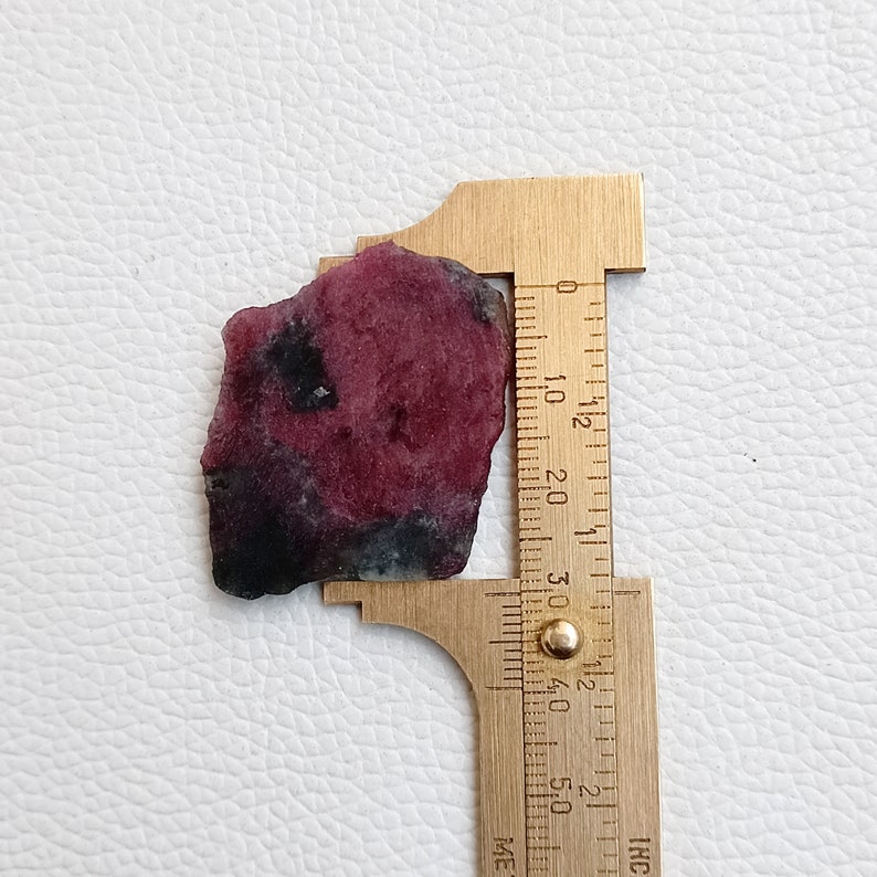 Może przedstawiać: Zbliżenie r&oacute;żowo-czarnego kamienia szlachetnego z linijką mierzącą około 3,8 cm długości.