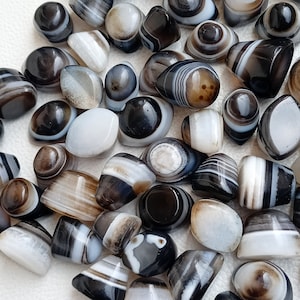 May include: A collection of banded agate stones in various shades of black, white, and brown. The stones are smooth and polished, with a variety of patterns and textures.