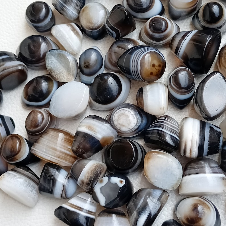 May include: A collection of banded agate stones in various shades of black, white, and brown. The stones are smooth and polished, with a variety of patterns and textures.