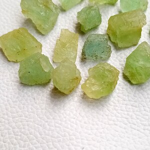 May include: A collection of small, rough, green and yellow gemstones. The stones are various shades of green and yellow, and some have a translucent quality.