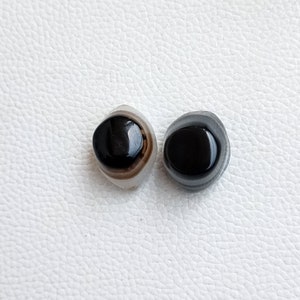 May include: Two black and white agate cabochons with a black center. The cabochons are smooth and polished.