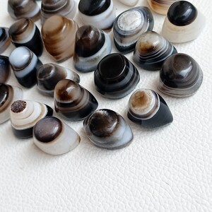 May include: A collection of banded agate stones, each with unique patterns of black, white, and brown stripes. The stones are smooth and polished, with a glossy finish.