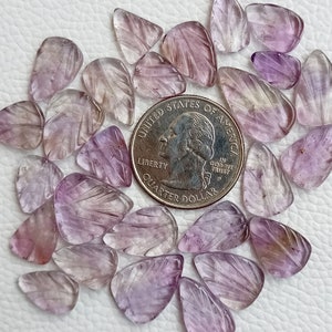 May include: A collection of 20 amethyst leaf shaped cabochons, each with a unique purple and white colour variation. The cabochons are arranged around a UK 20 pence coin for size reference.