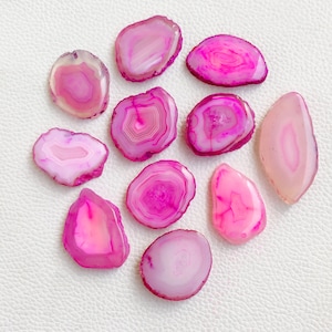 May include: Assortment of pink agate slices with varying patterns and shapes. The agate slices are smooth and polished, with a natural, organic look.