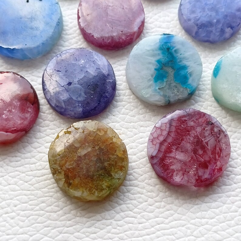 May include: Assortment of round agate slices in various colors and patterns, including pink, blue, purple, and brown. The agate slices are polished and have a smooth, shiny surface.