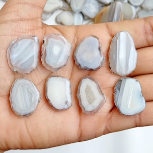 May include: Eight white agate slices with gray banding, showing the natural crystal formations. The slices are smooth and polished, with a translucent appearance.