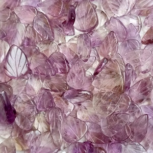 May include: A large pile of purple amethyst leaf-shaped beads. The beads are carved with intricate details and have a translucent appearance.
