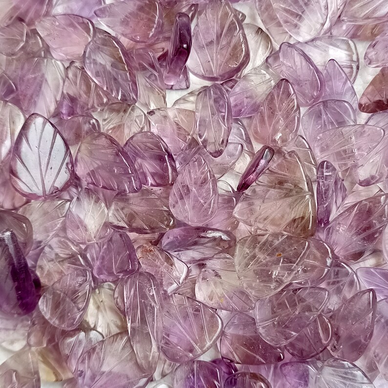 May include: A large pile of purple amethyst leaf-shaped beads. The beads are carved with intricate details and have a translucent appearance.