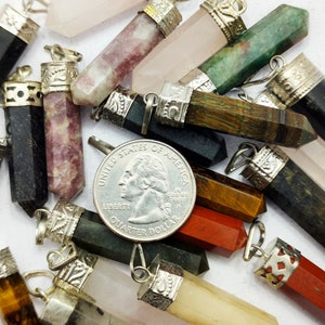 May include: A collection of 14 gemstone pendants with silver caps. The pendants are in various colours, including black, brown, green, red, pink, and purple. A UK 20 pence coin is included for scale.