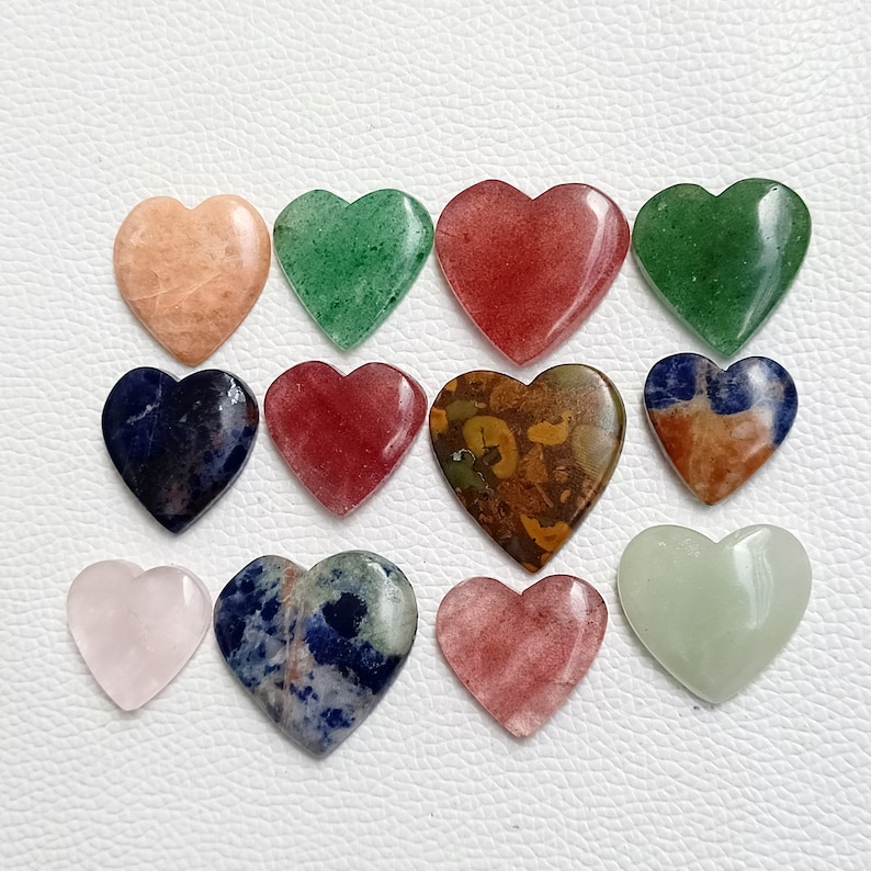May include: Assortment of 14 heart-shaped polished stones in various colors, including pink, red, green, blue, and brown. The stones are arranged in a grid pattern on a white surface.