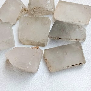 May include: A collection of raw, translucent quartz crystal chunks. The crystals vary in shape, with some appearing rectangular and others more irregular. The color is a pale, milky white with subtle variations and natural inclusions.