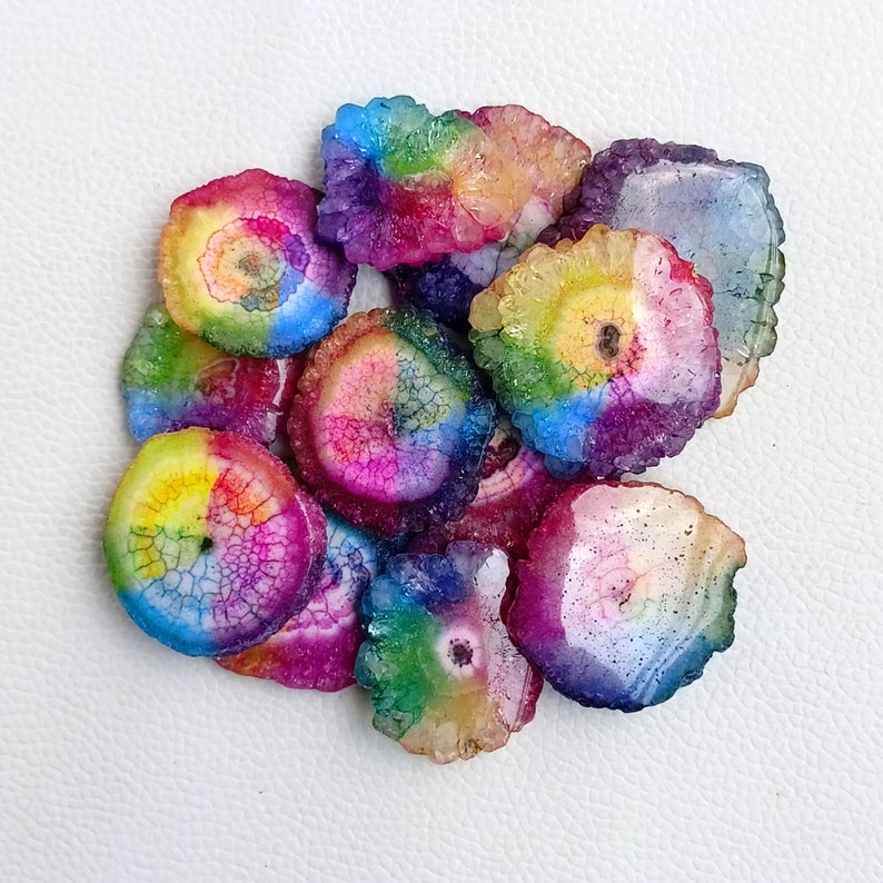 May include: A collection of rainbow agate slices, each with a unique pattern of colors and textures. The slices are arranged in a pile, with the colors blending together to create a vibrant and colorful display.